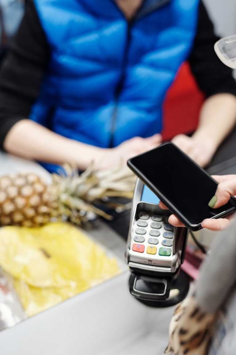 A customer uses a smartphone for contactless payment at a retail checkout with fresh produce.