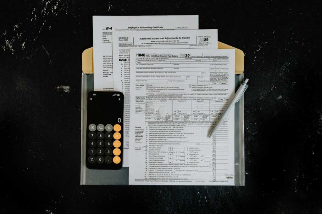 Tax forms with calculator and pen on dark surface