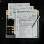 Tax forms with calculator and pen on dark surface