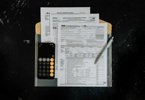 Tax forms with calculator and pen on dark surface